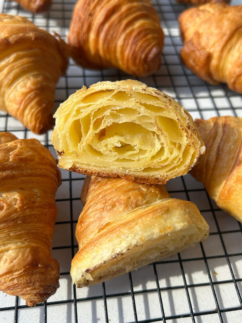 Croissants on a cooling rack with one cut open to show layers.