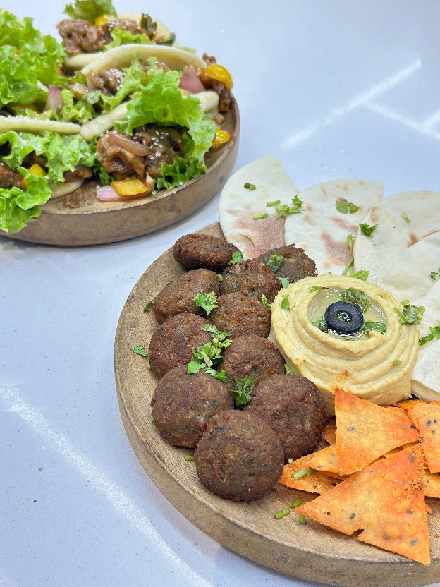 Platter of falafel with hummus, pita, and chips on a light blue surface at 'La Bake Amore' Delhi