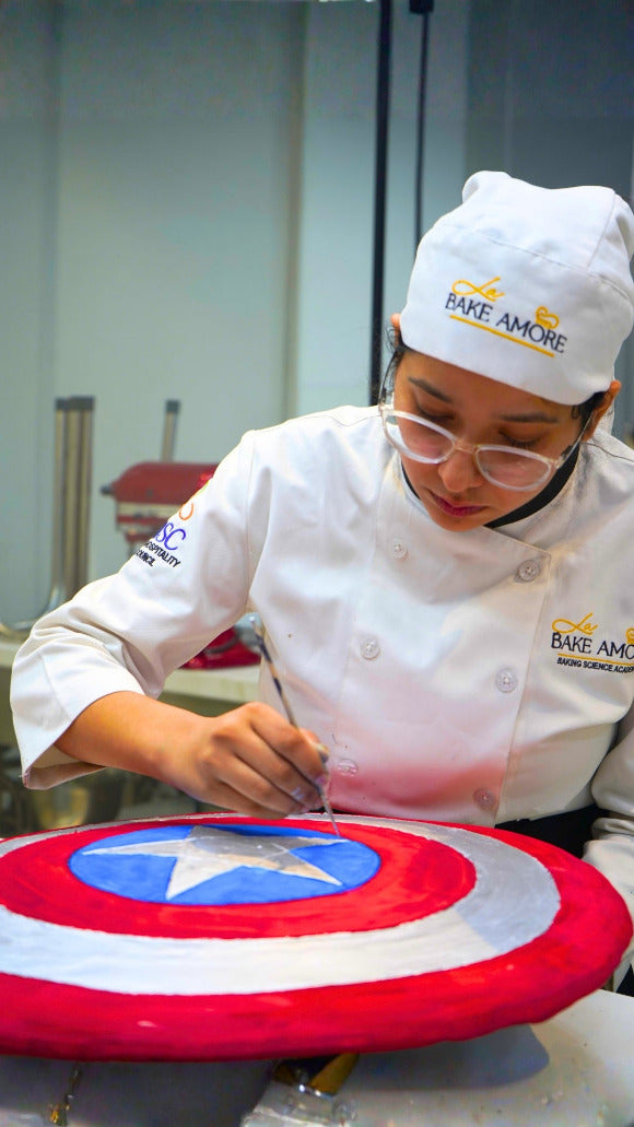 Chef decorating a cake shaped like Captain America's shield in a kitchen setting.
