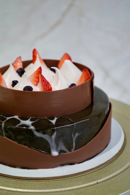 Two-tiered chocolate cake with strawberries and cream on a white plate.