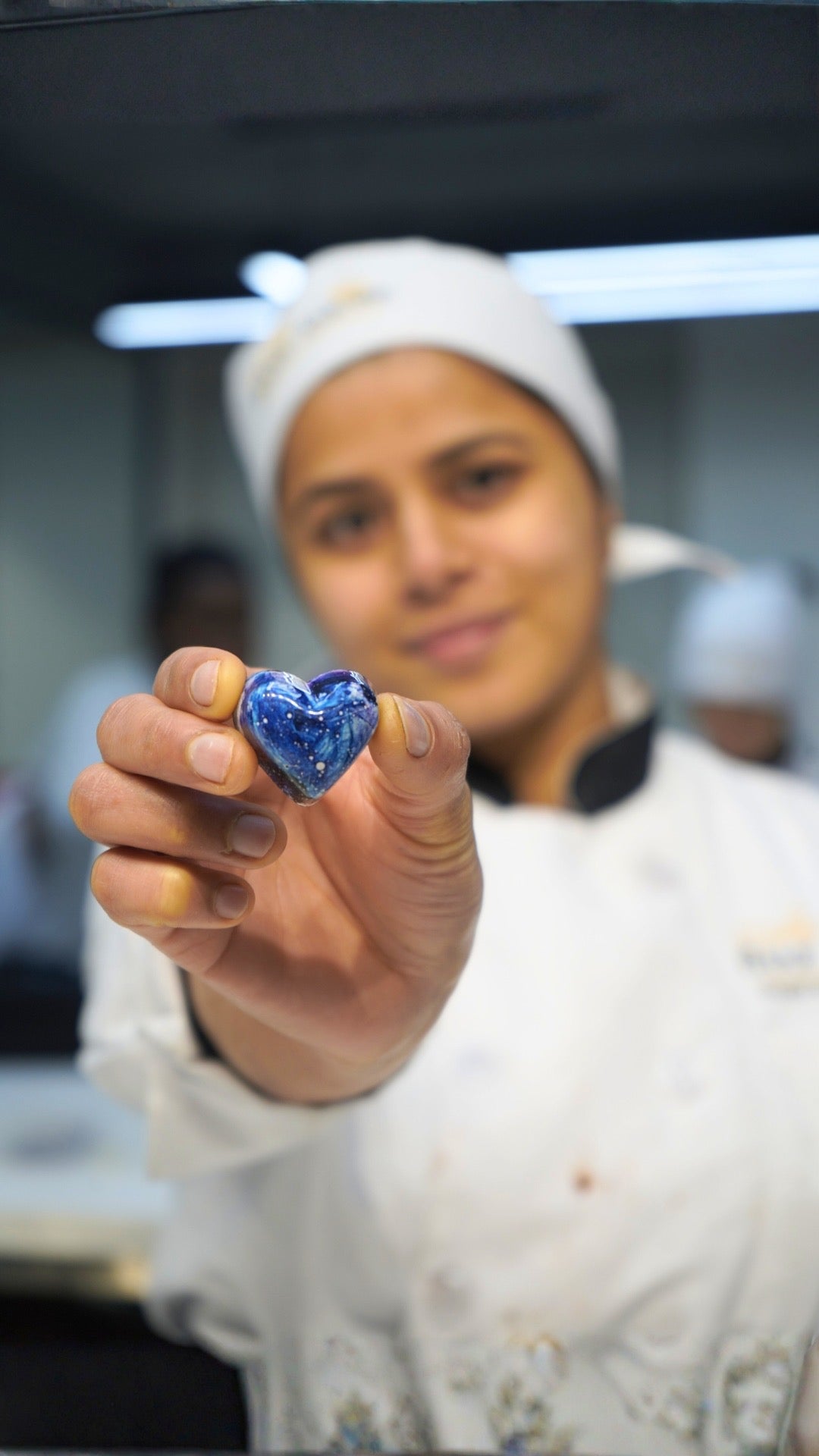 Person holding a blue heart-shaped chocolate in a kitchen setting
