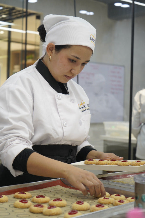 Person in a chef's uniform with a tray of cookies in a kitchen setting
