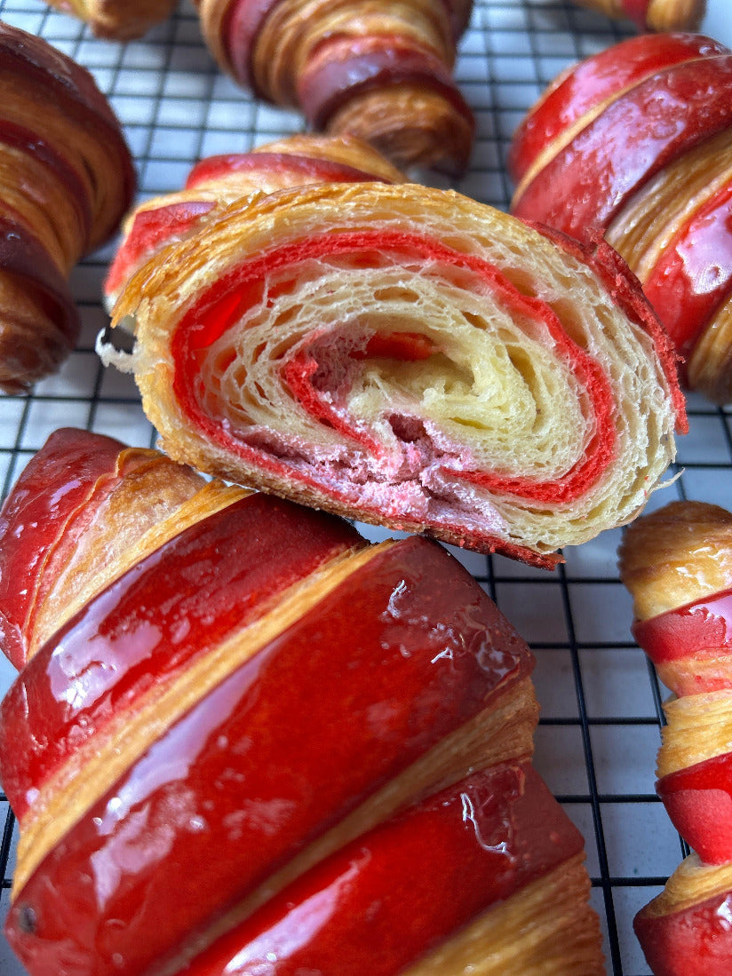 Close-up of red and yellow croissants on a cooling rack.