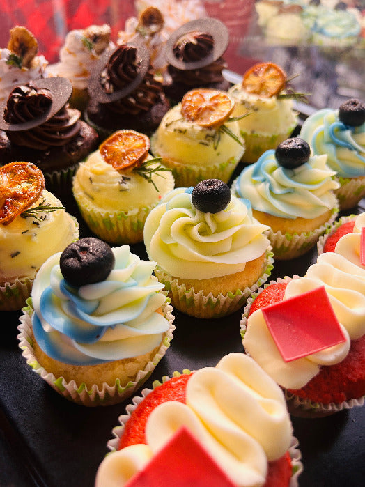 Assorted cupcakes with various flavors and decorations on a black tray.