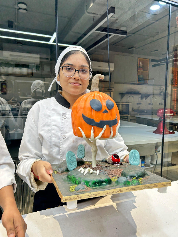 Person holding a Halloween-themed cake with a pumpkin face in a kitchen setting