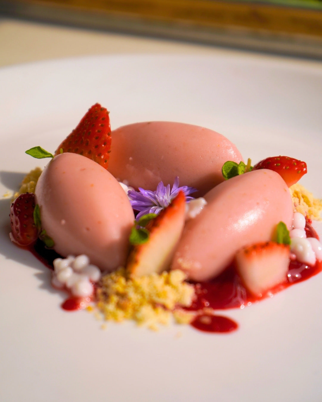 Delicate dessert with pink mousse, strawberries, and purple flowers on a white plate.