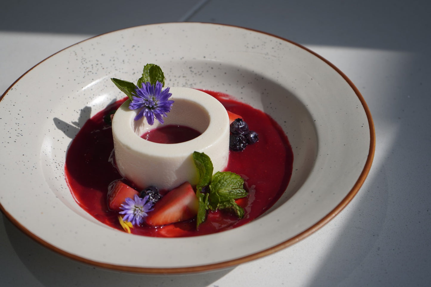 Delicate dessert with white cream, red sauce, and garnishes on a white plate.